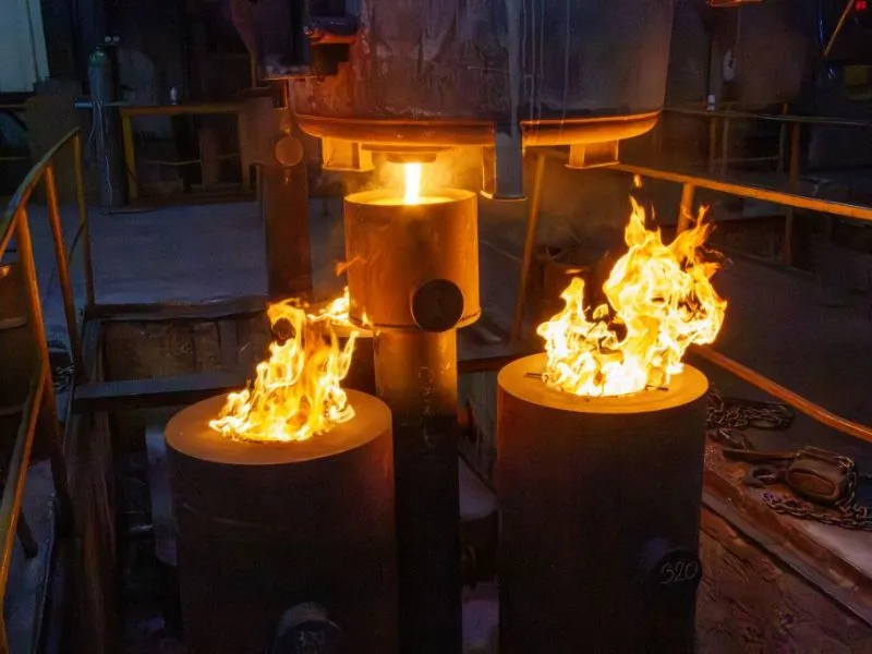 Glühendes Metall fließt in zylinderförmige Formen, aus denen Flammen aufsteigen – eindrucksvoller Herstellungsprozess von Gussteilen in einer industriellen Gießerei.